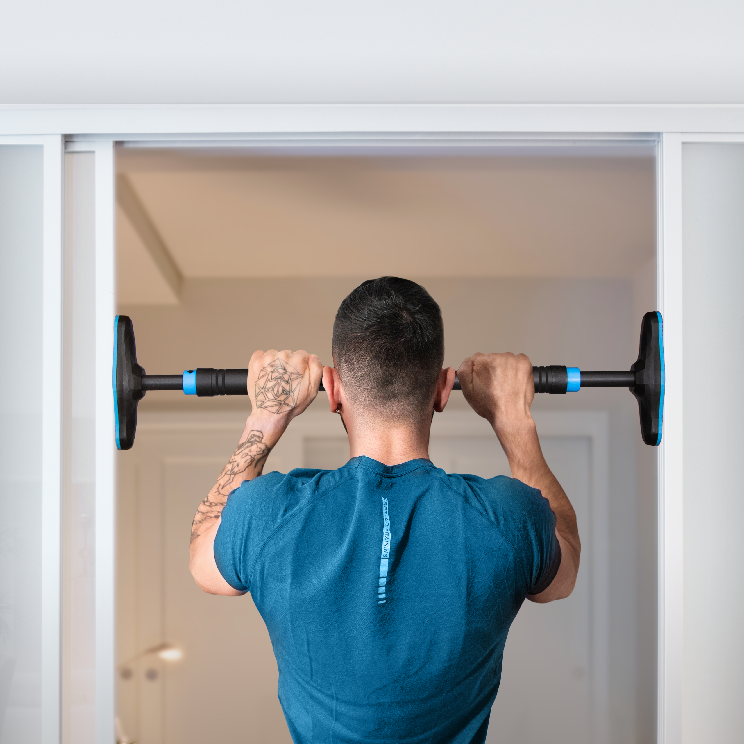 Ein Mann führt Klimmzüge an einer an einem Türrahmen montierten Neolymp-Klimmzugstange durch. Er trägt ein blaues T-Shirt und zeigt ein Tattoo auf seinem rechten Arm. Die Klimmzugstange ist mit blauen Enden ausgestattet, die für Stabilität sorgen.